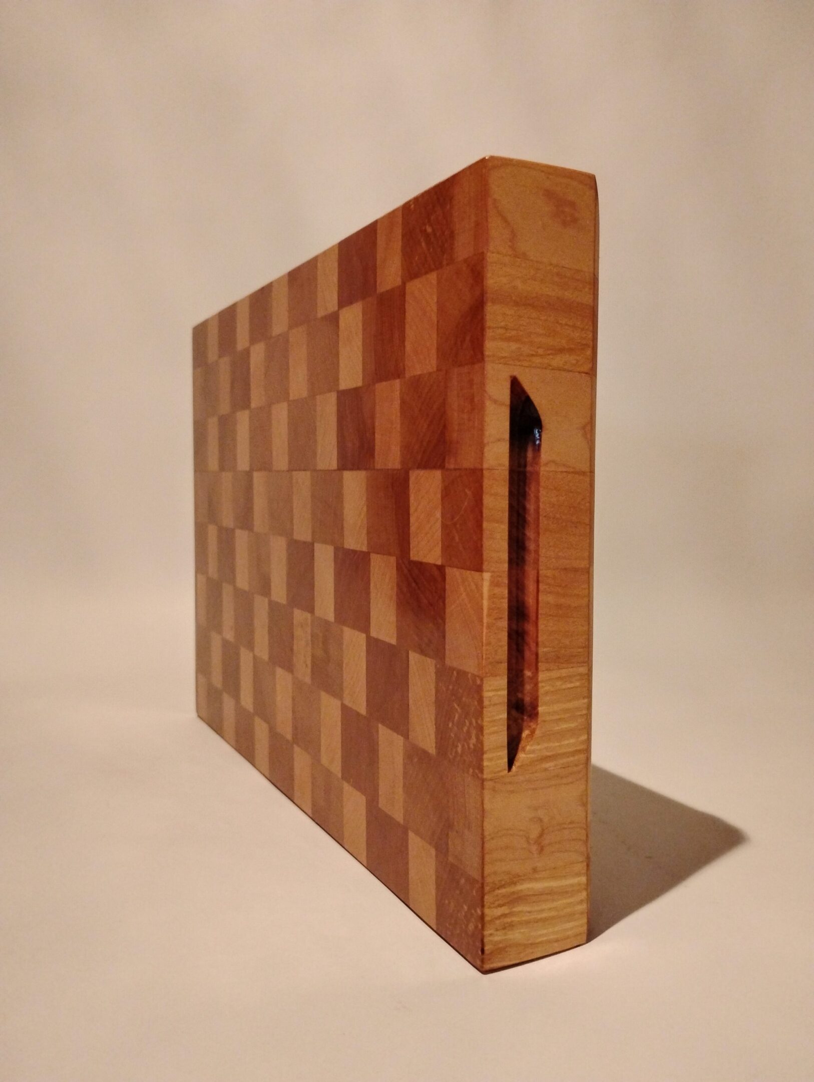 Wooden end-grain cutting board with a checkered pattern and slot for a knife.