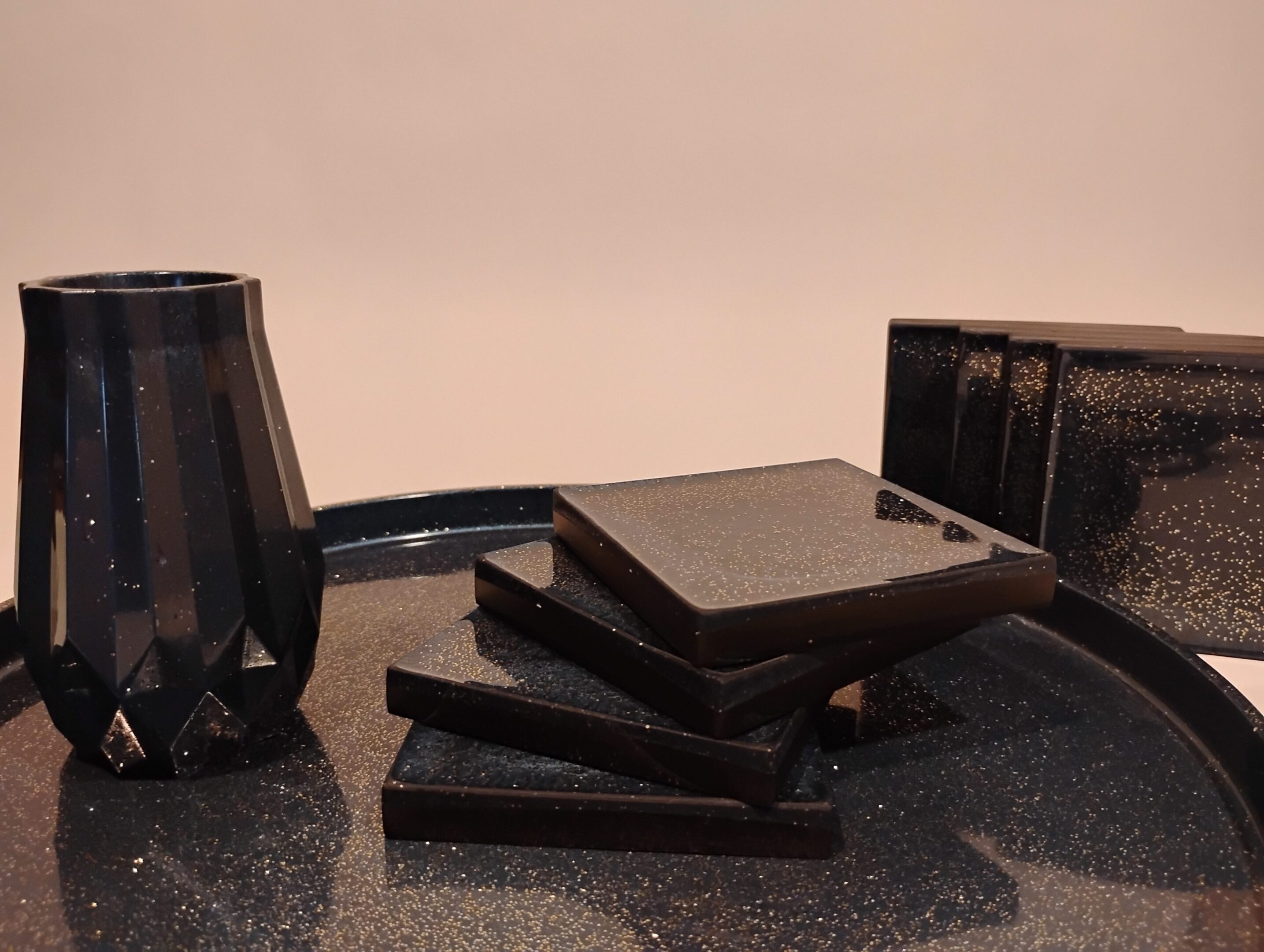 Stacked black square plates and a black vase on a reflective surface.