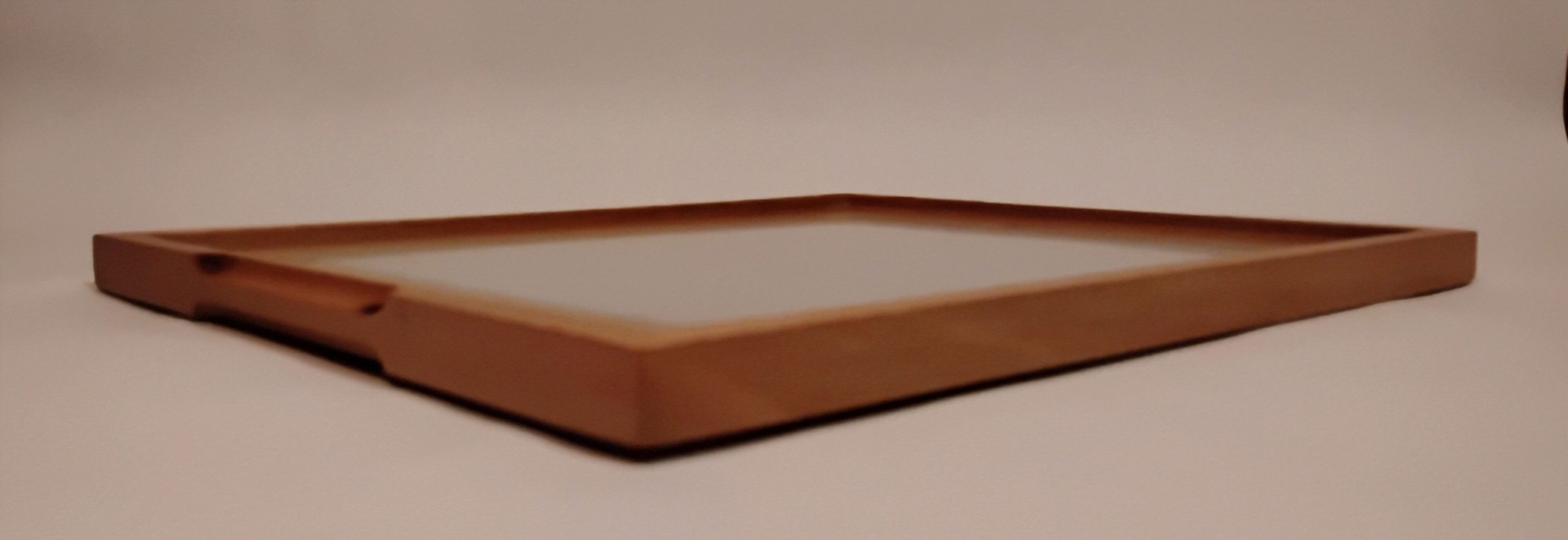 Close-up of a wooden tray with raised edges on a light surface.