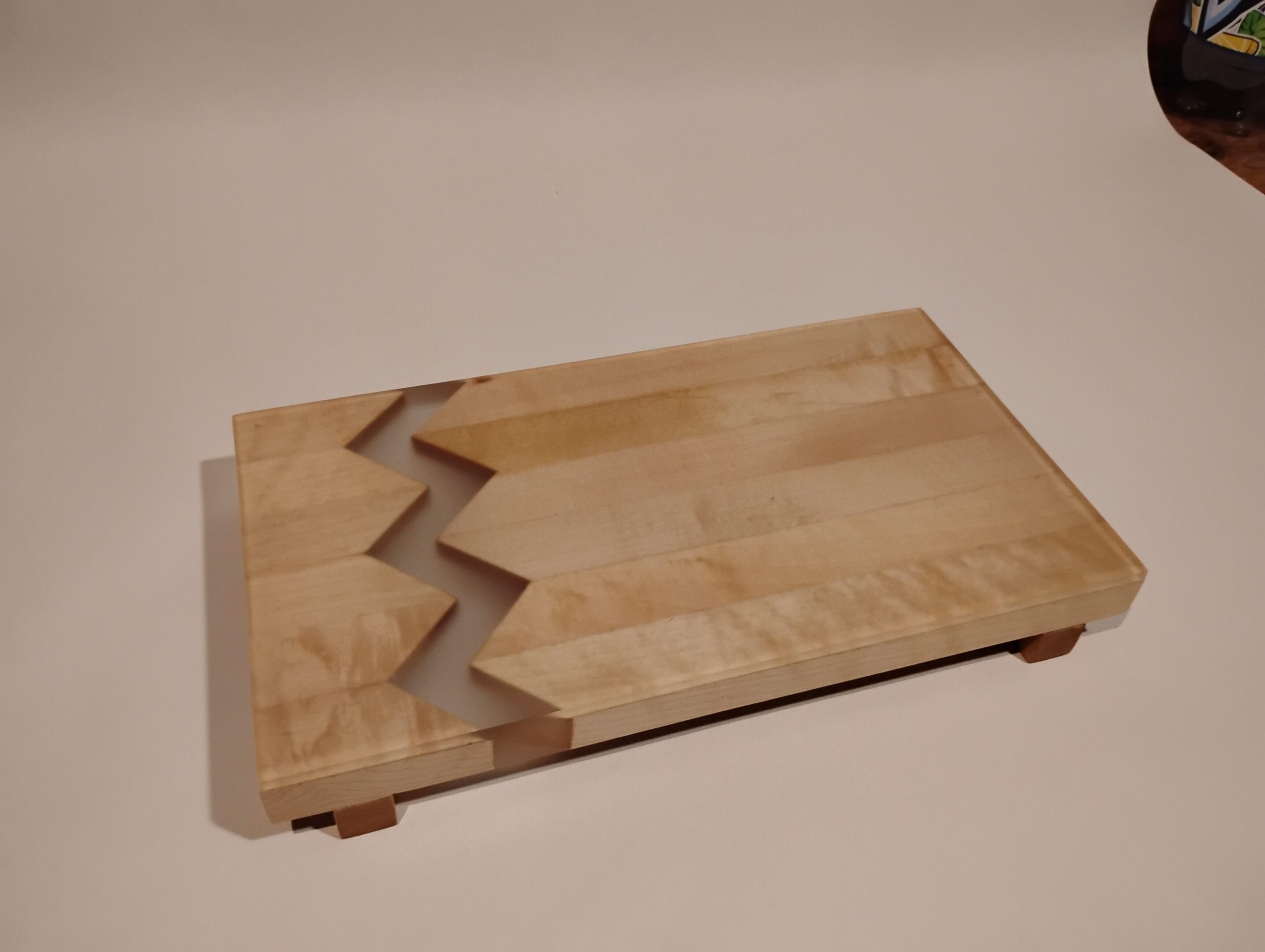 Wooden cutting board with a zigzag pattern and corner feet.