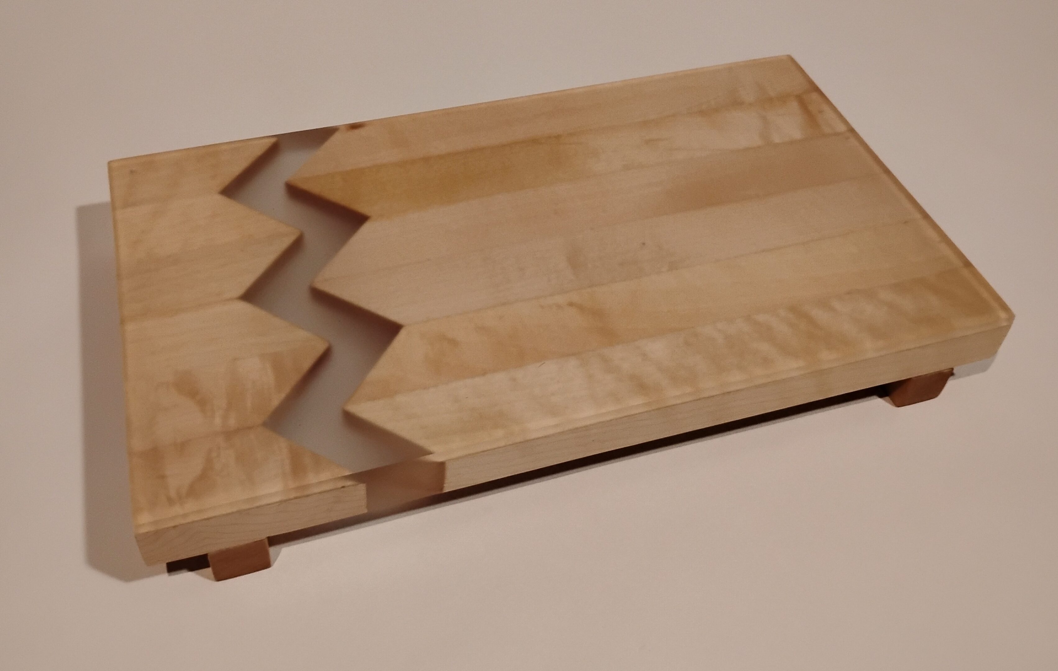 A wooden serving board with geometric, zigzag inlay design.