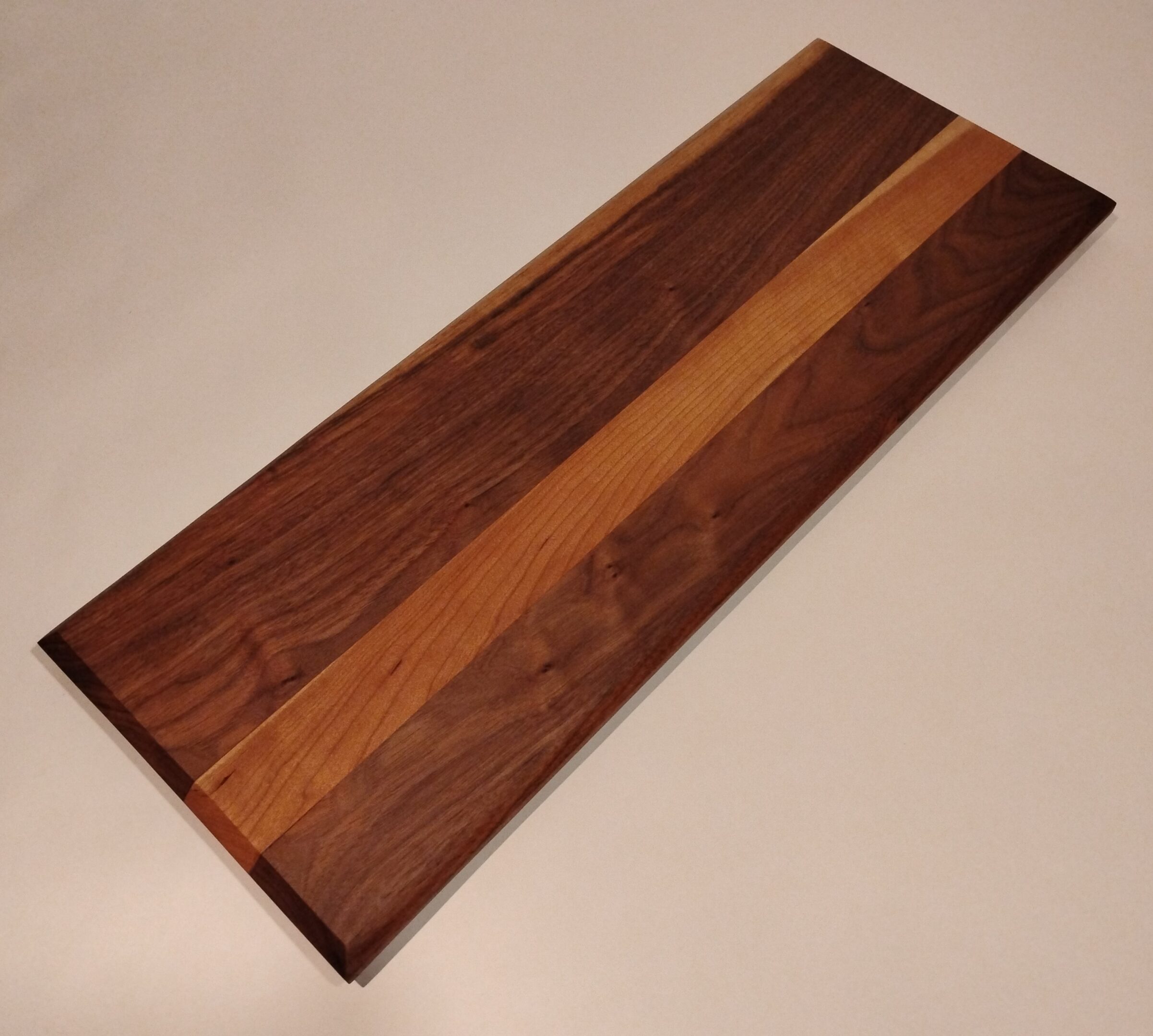 A rectangular wooden cutting board with mixed wood tones.