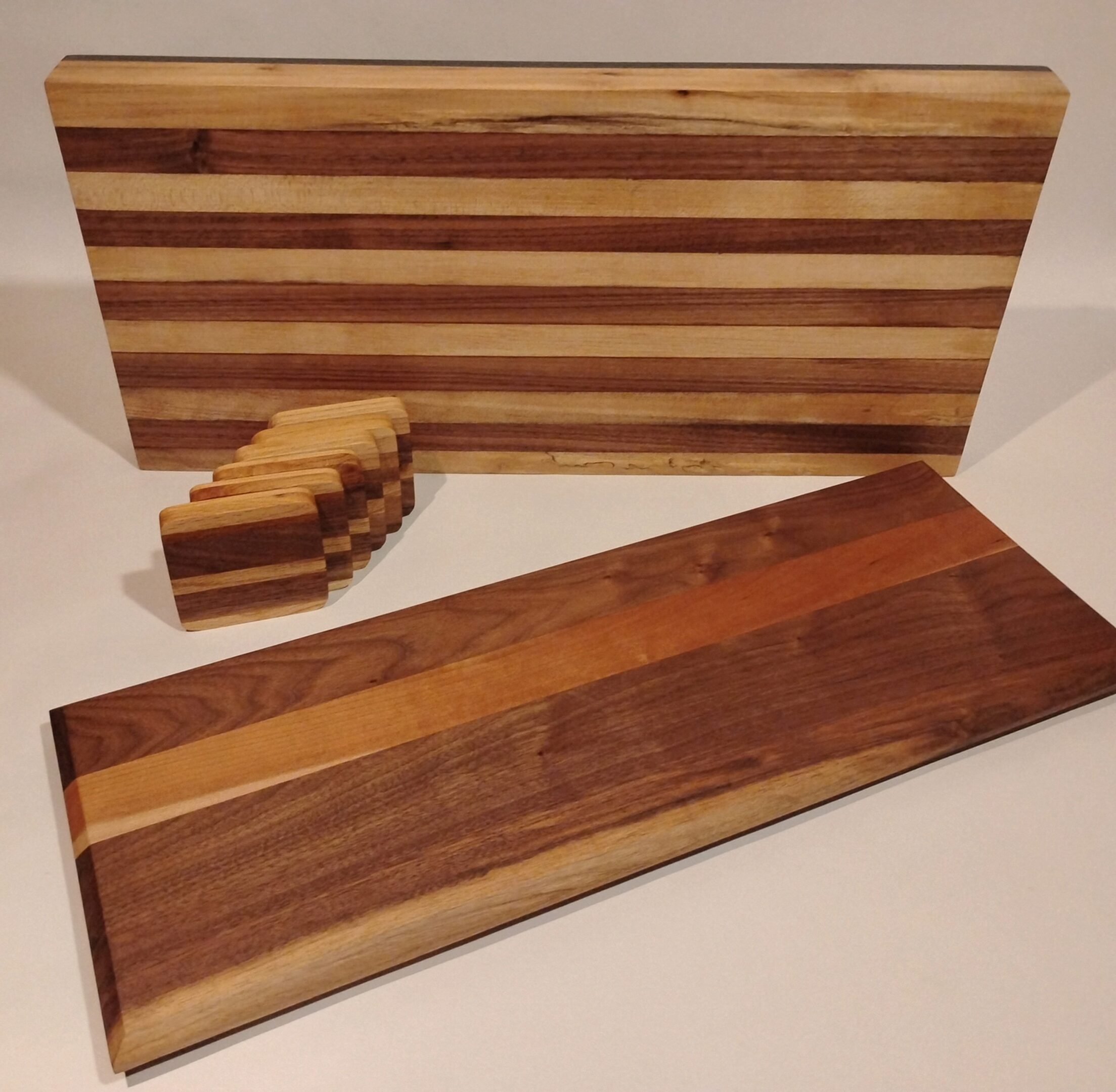 Two wooden cutting boards with striped patterns and matching wooden coasters.