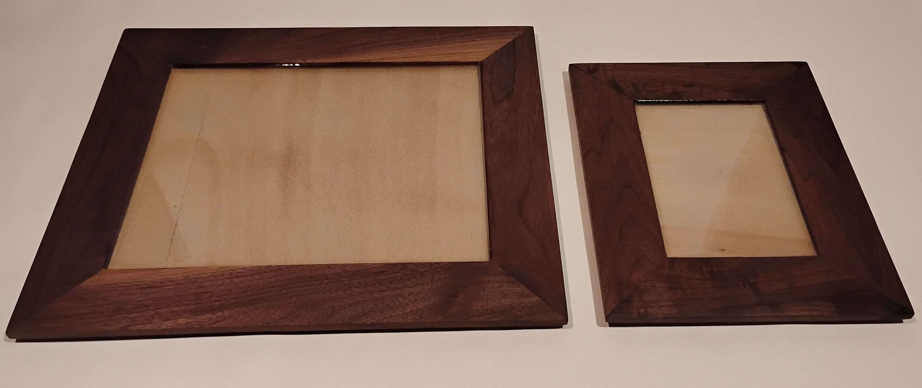 Two wooden frames with dark brown borders, empty and placed on a light surface.