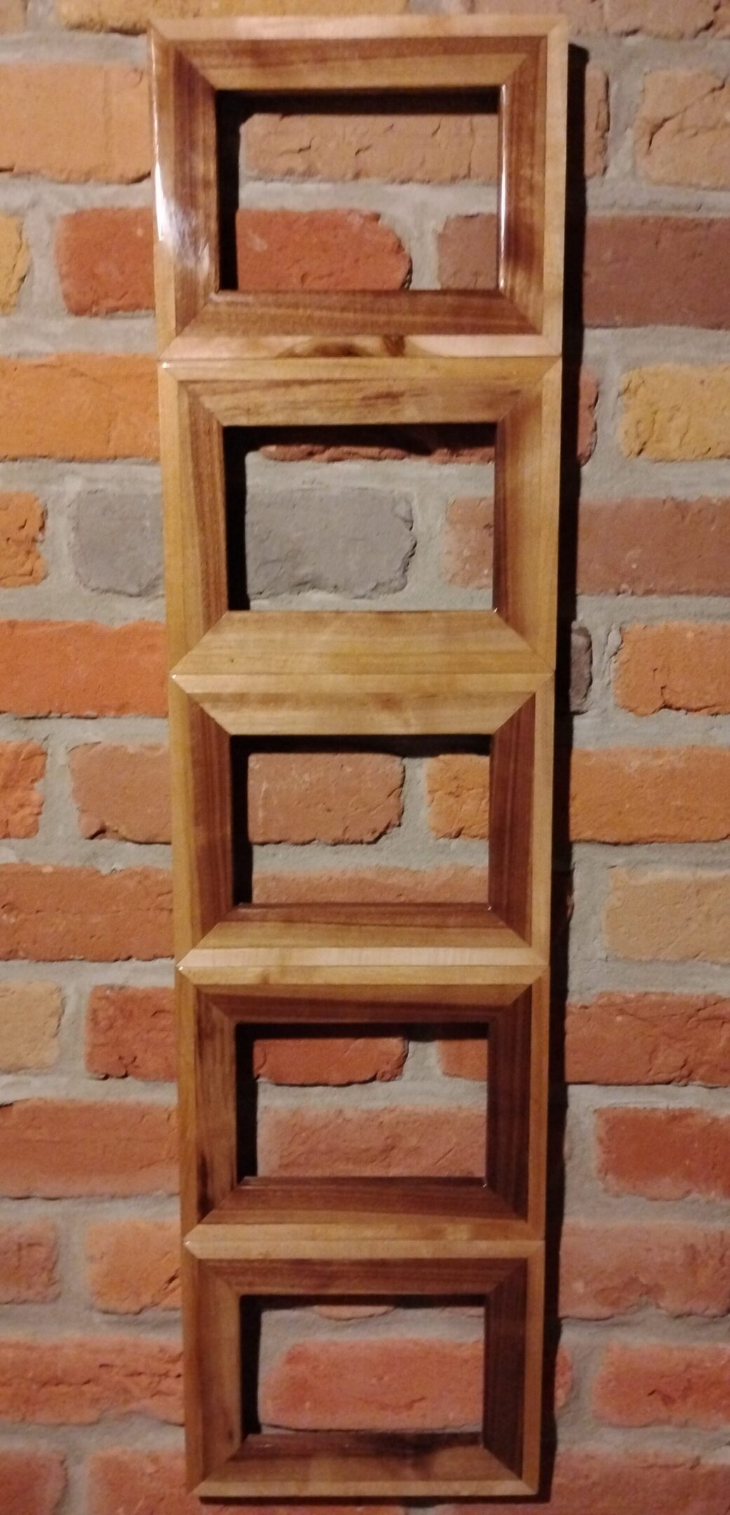 Three wooden frames mounted vertically on a brick wall.