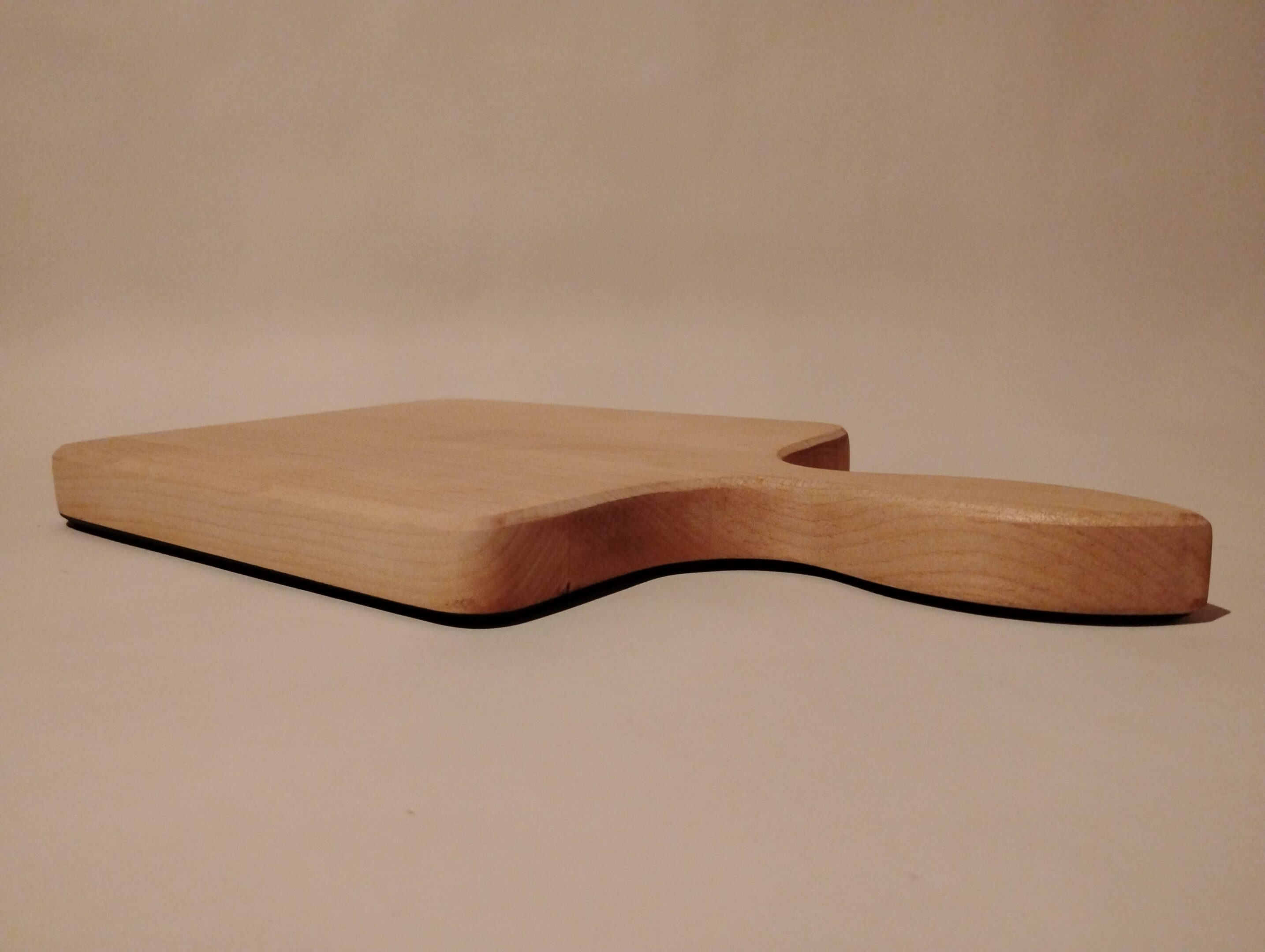 A wooden cutting board with a handle on a plain surface.