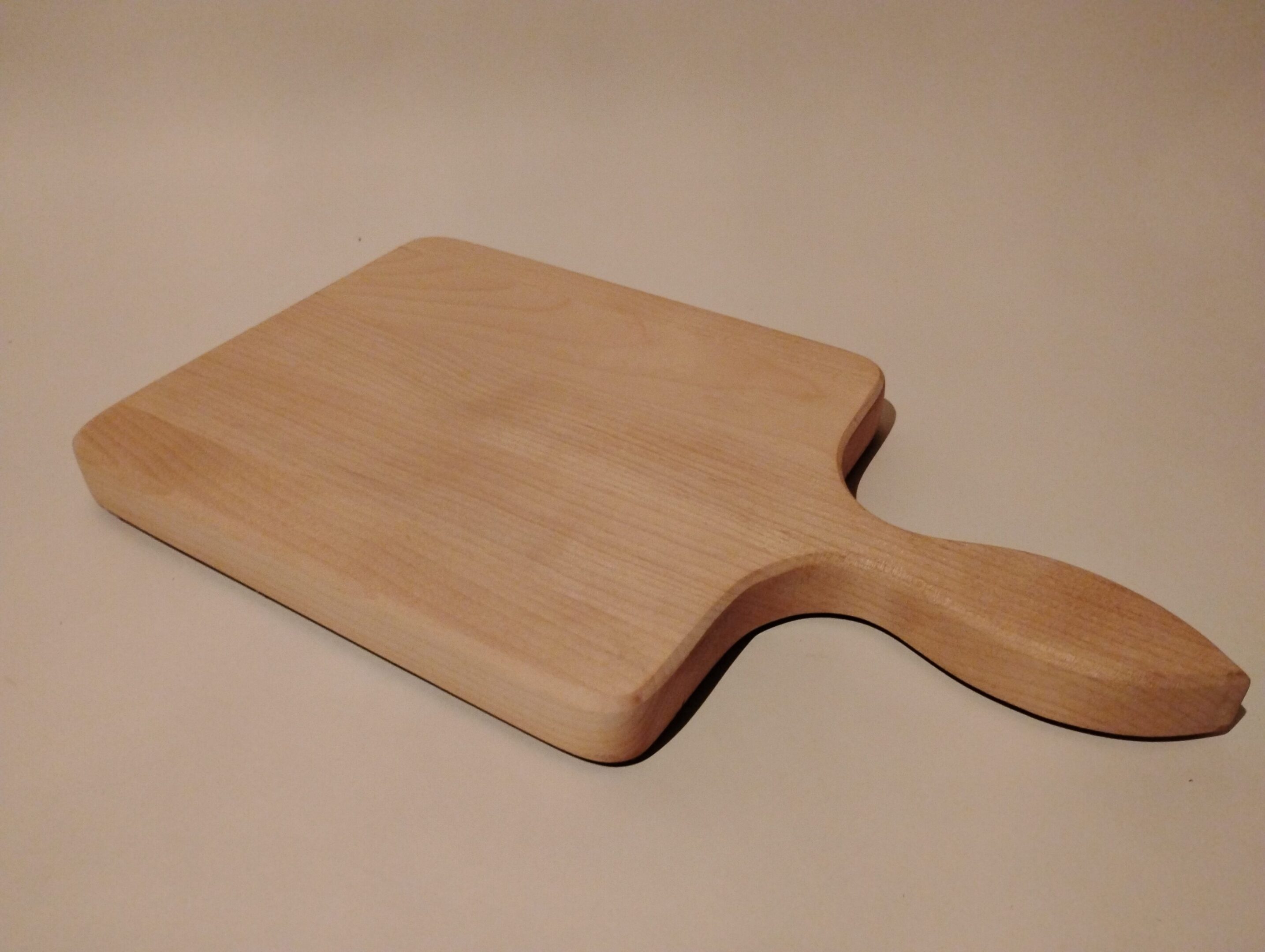 Wooden cutting board with handle on a neutral background.