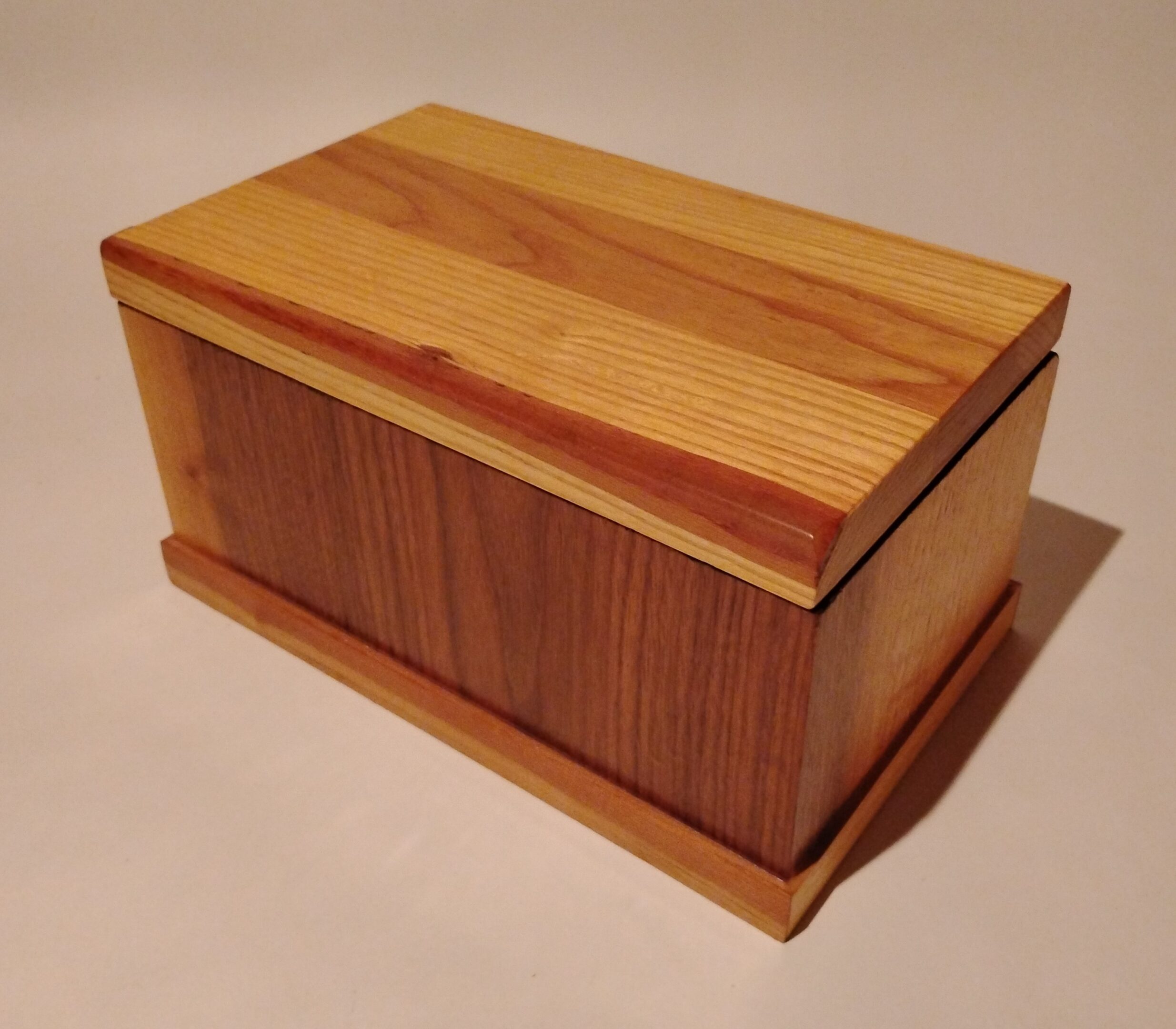 A polished wooden box with a hinged lid on a light surface.