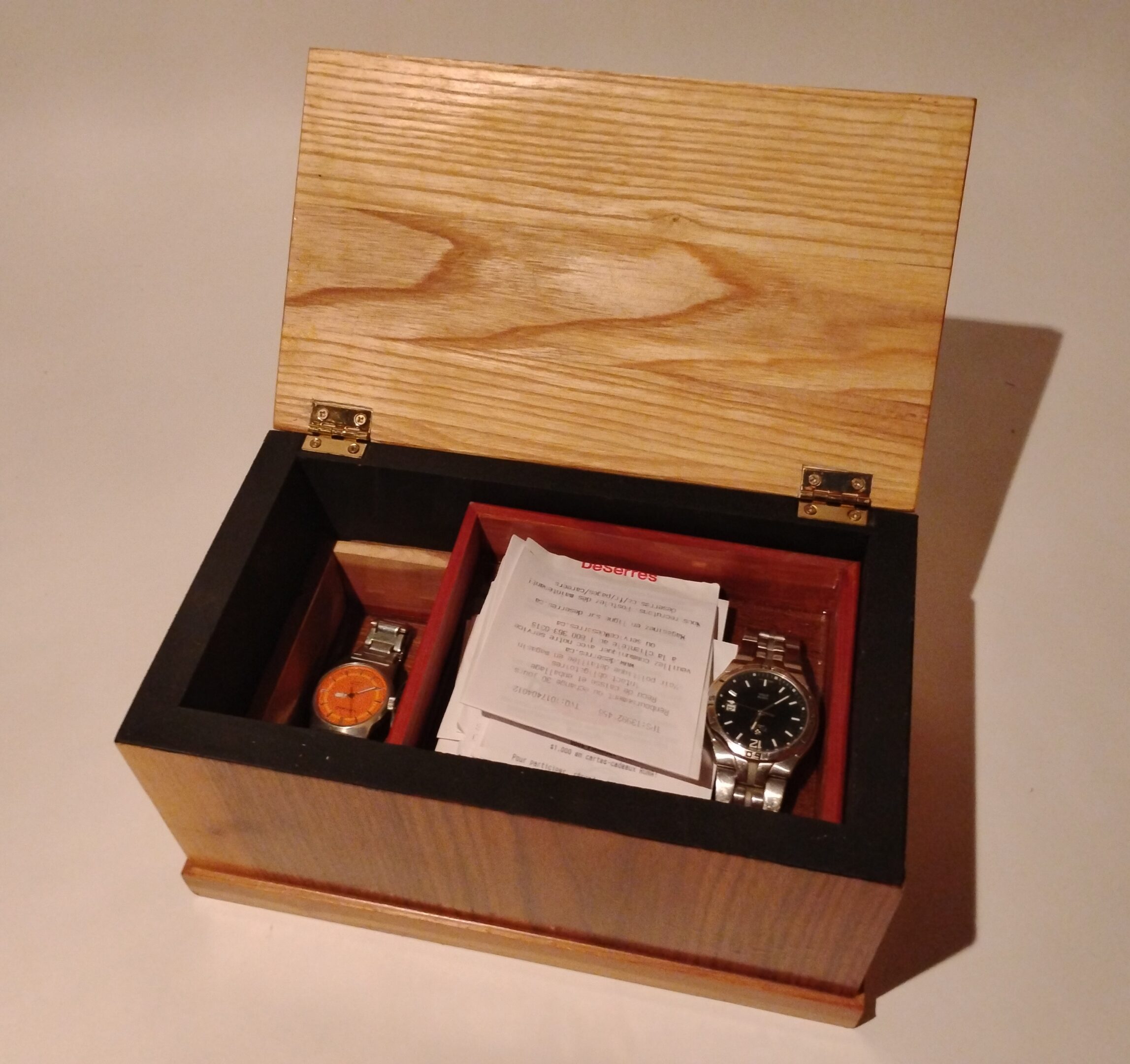 Wooden box containing a wristwatch, paperwork, and accessories.