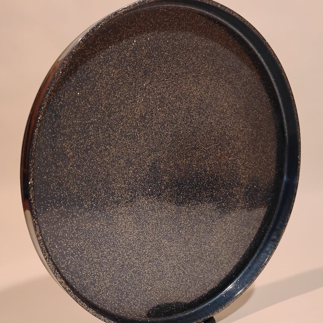 Round black tray with textured surface on a beige background.