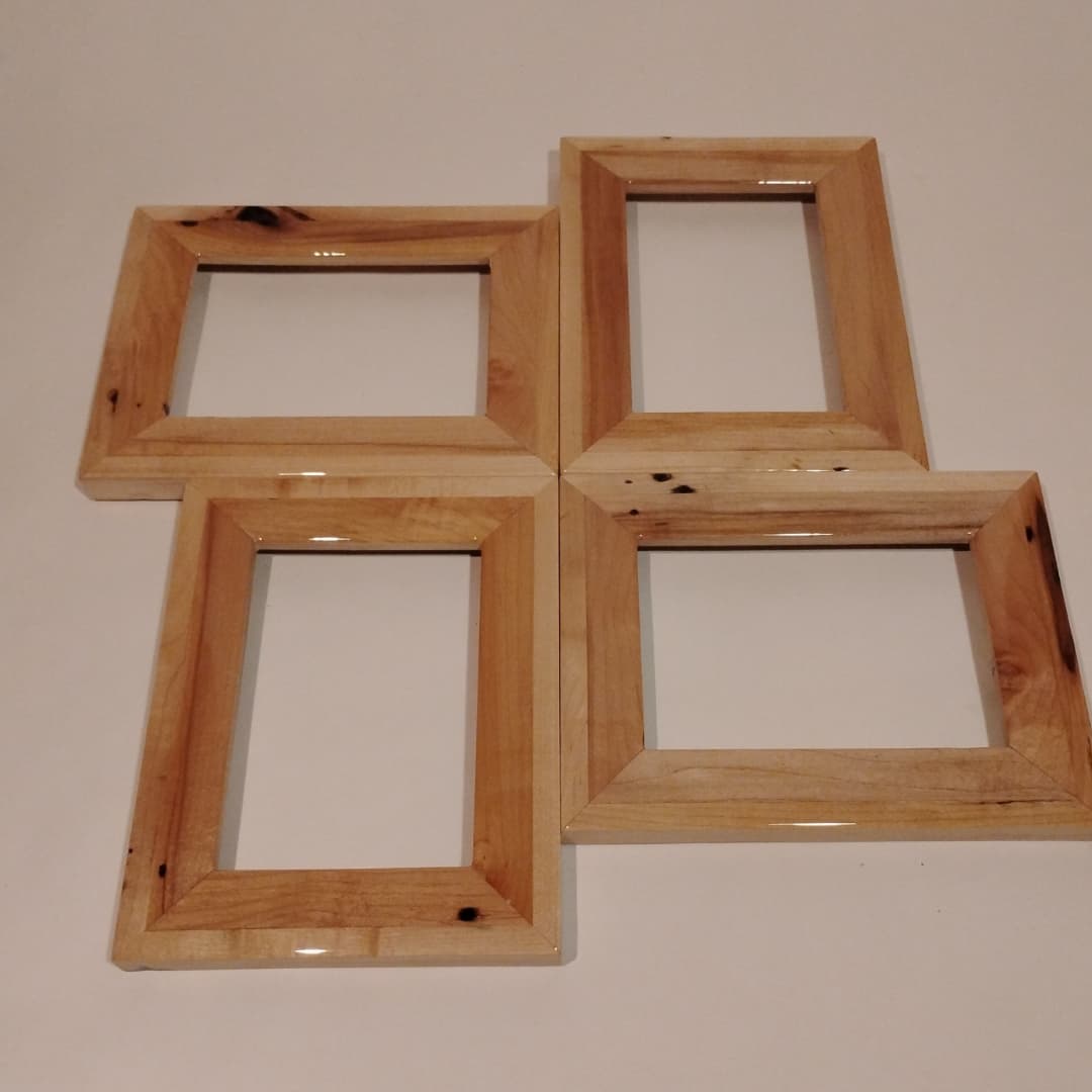A set of four empty wooden picture frames arranged in a plus shape.