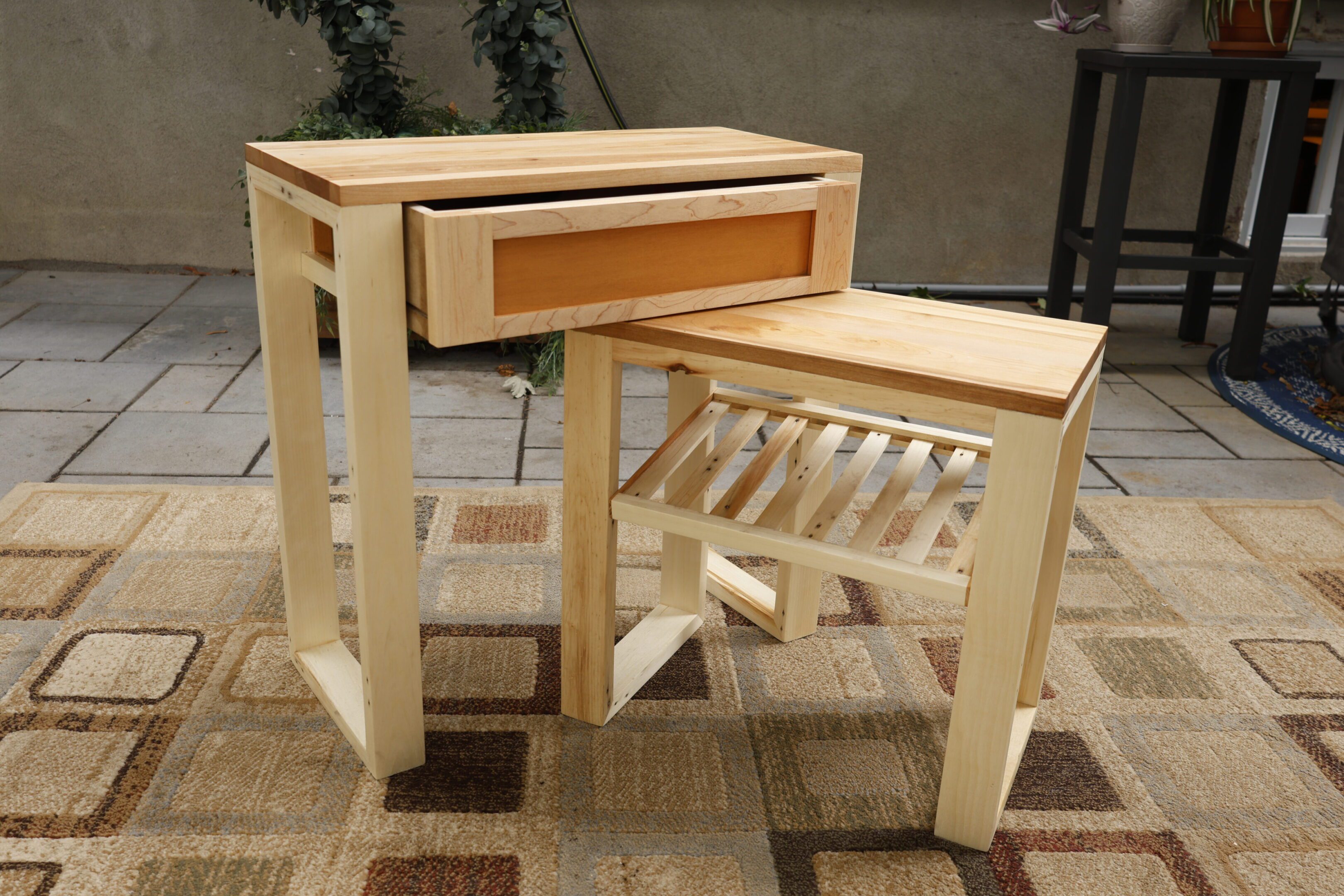 Wooden side table with a drawer and matching stool on a patterned rug.