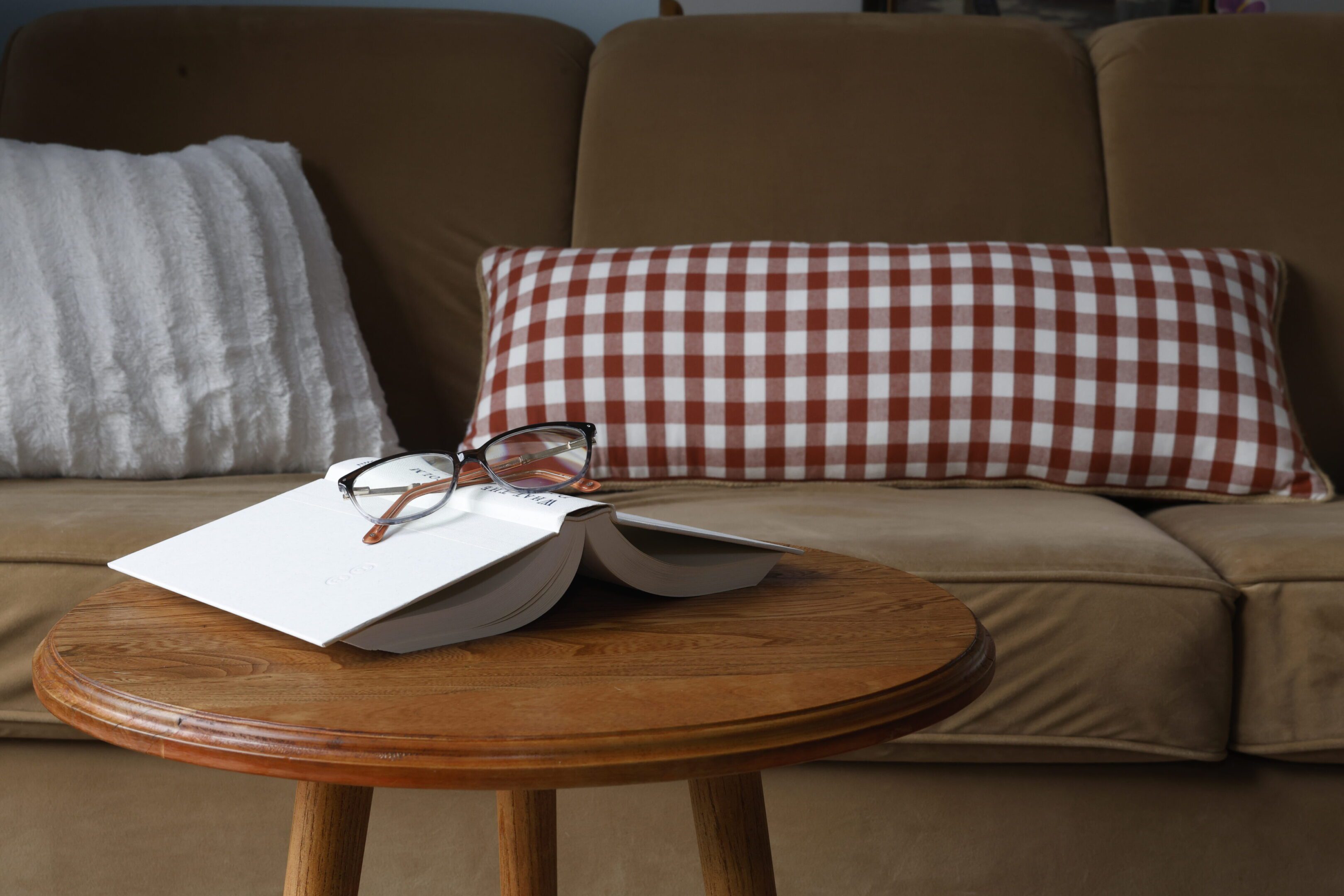 Open book and reading glasses on a wooden table in a cozy living room.