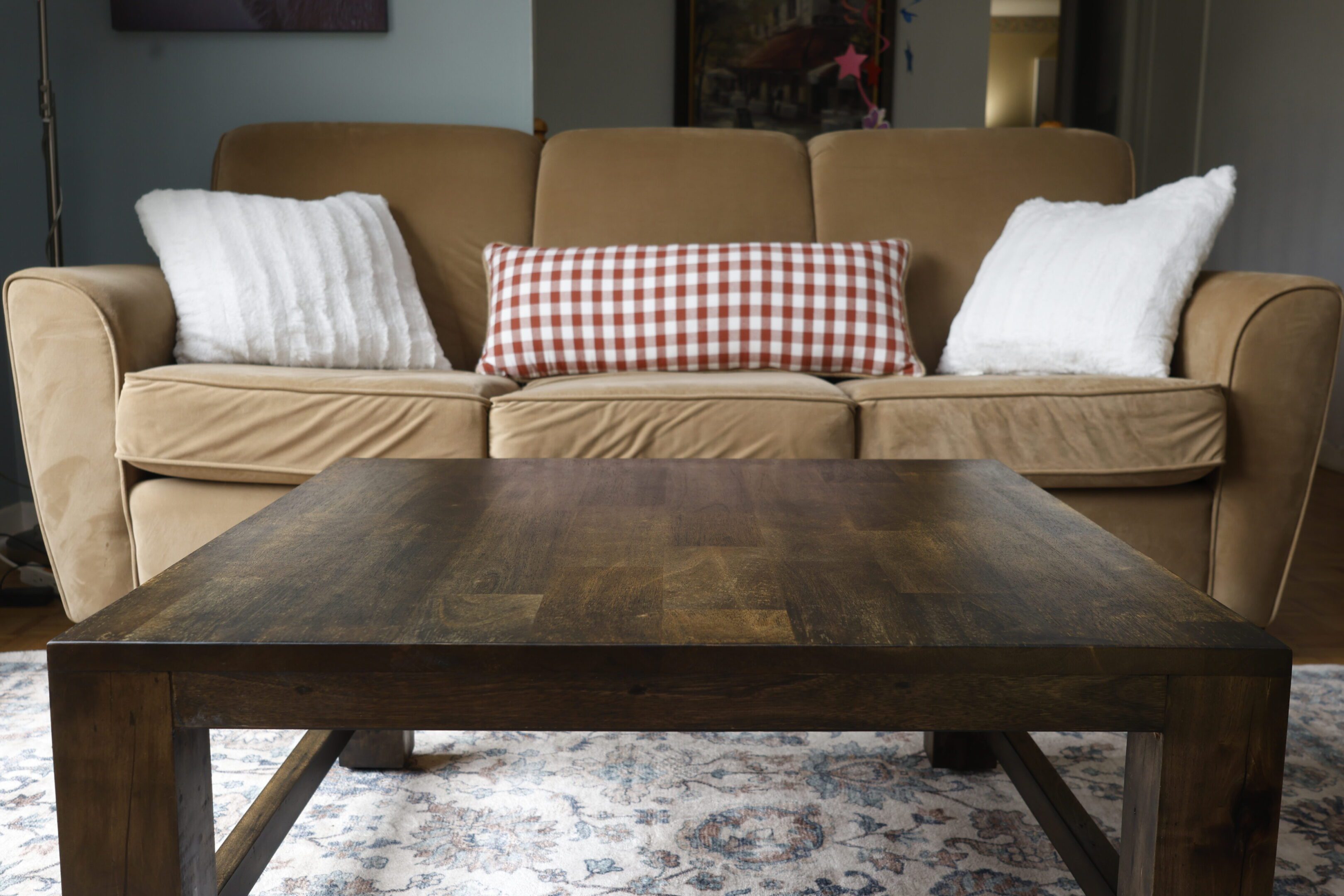 Wooden coffee table in front of a beige couch with cushions.