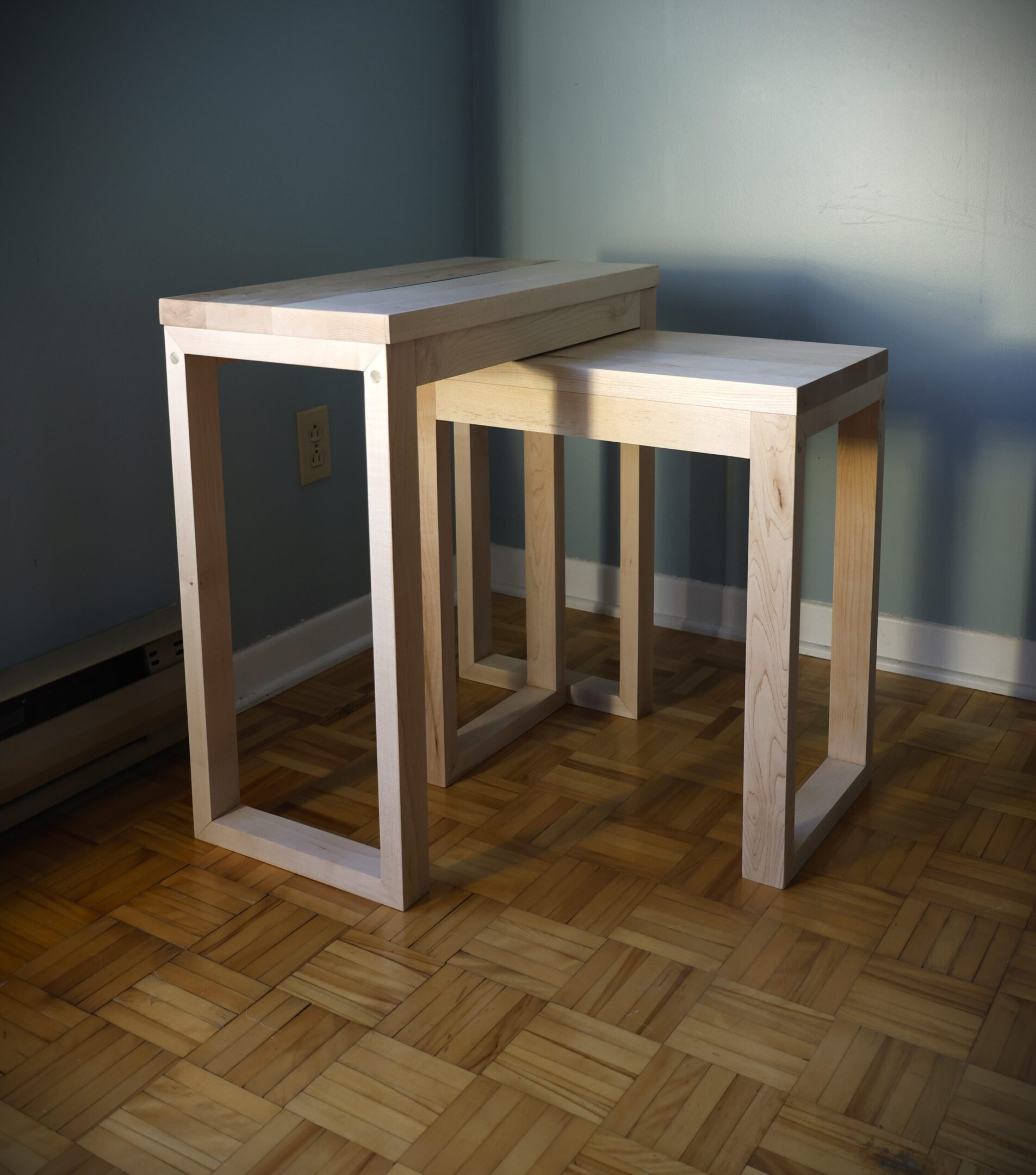Two nested wooden tables with glass tops in a minimalist room.
