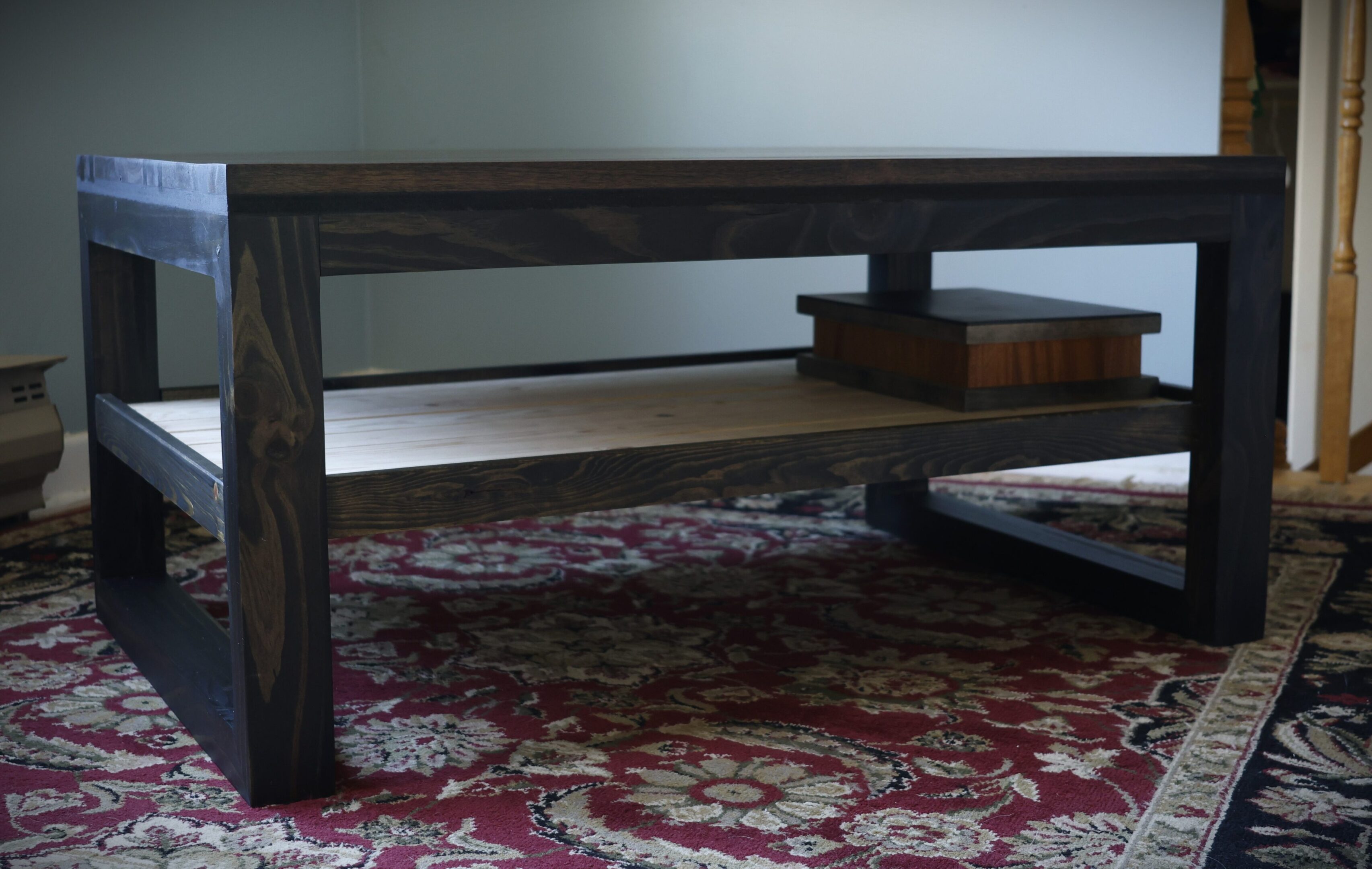 Dark wood coffee table with a lower shelf on a patterned rug.